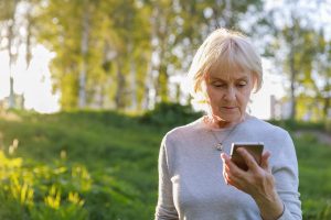 An elderly woman is holding a phone in her hand, looking concerned. She appears to be worried or distressed, possibly indicating a situation related to a delivery scam or another type of fraudulent activity.