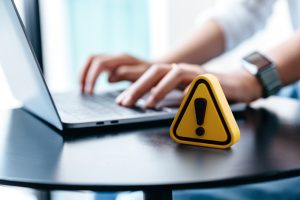 A warning sign is placed on a table while a person works on a computer in the background.
