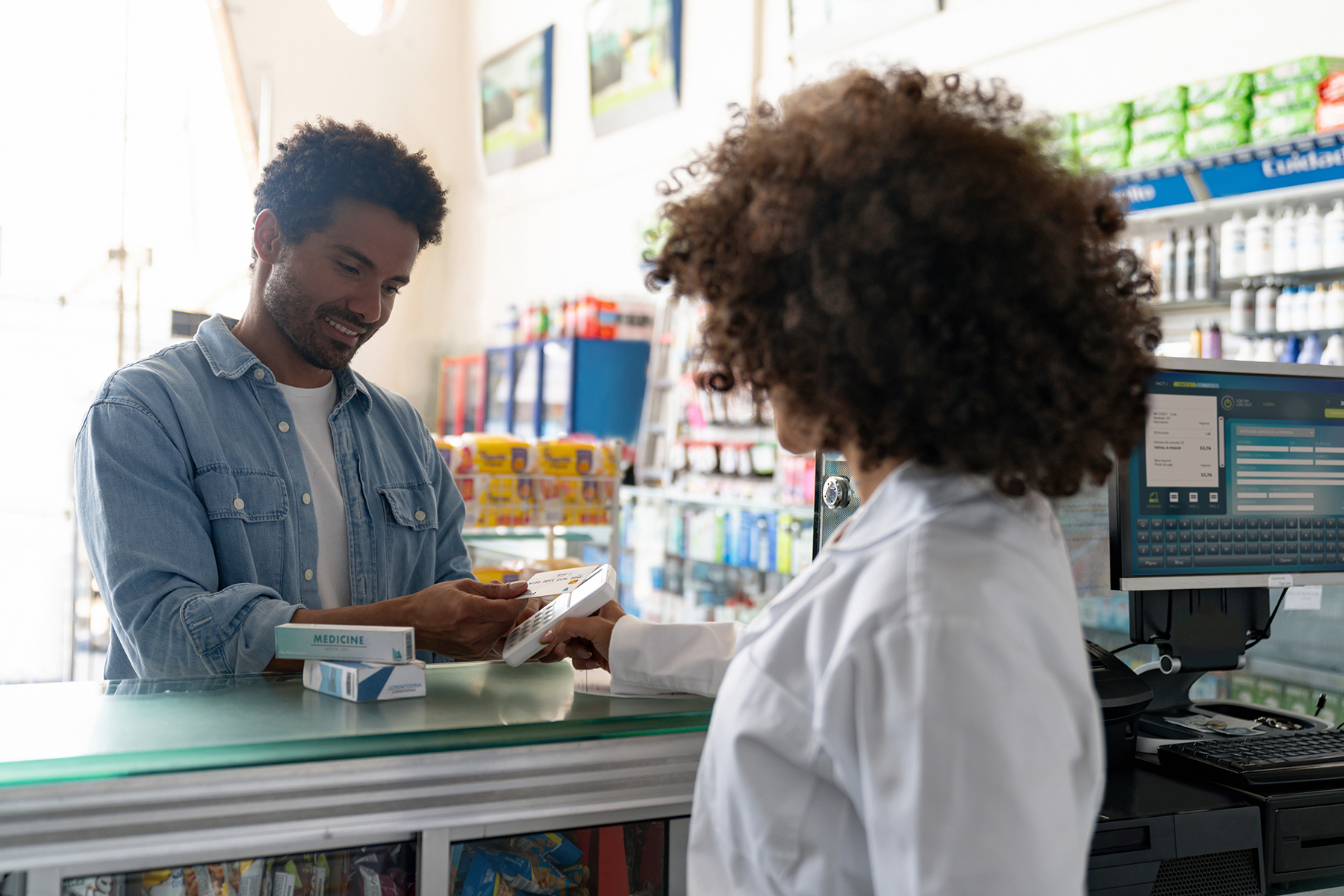 A man is making a payment while shopping for medicine at a pharmacy. The background includes blurred store shelves in a shopping environment.