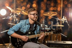 A musician is playing an electric guitar in a studio, illuminated by colorful stage lights. The background is dark, with vibrant light beams creating a dynamic and energetic atmosphere, emphasizing the creativity and passion of the performance.