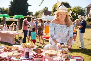 A woman in a hat is standing in front of a table serving food at an outdoor picnic.