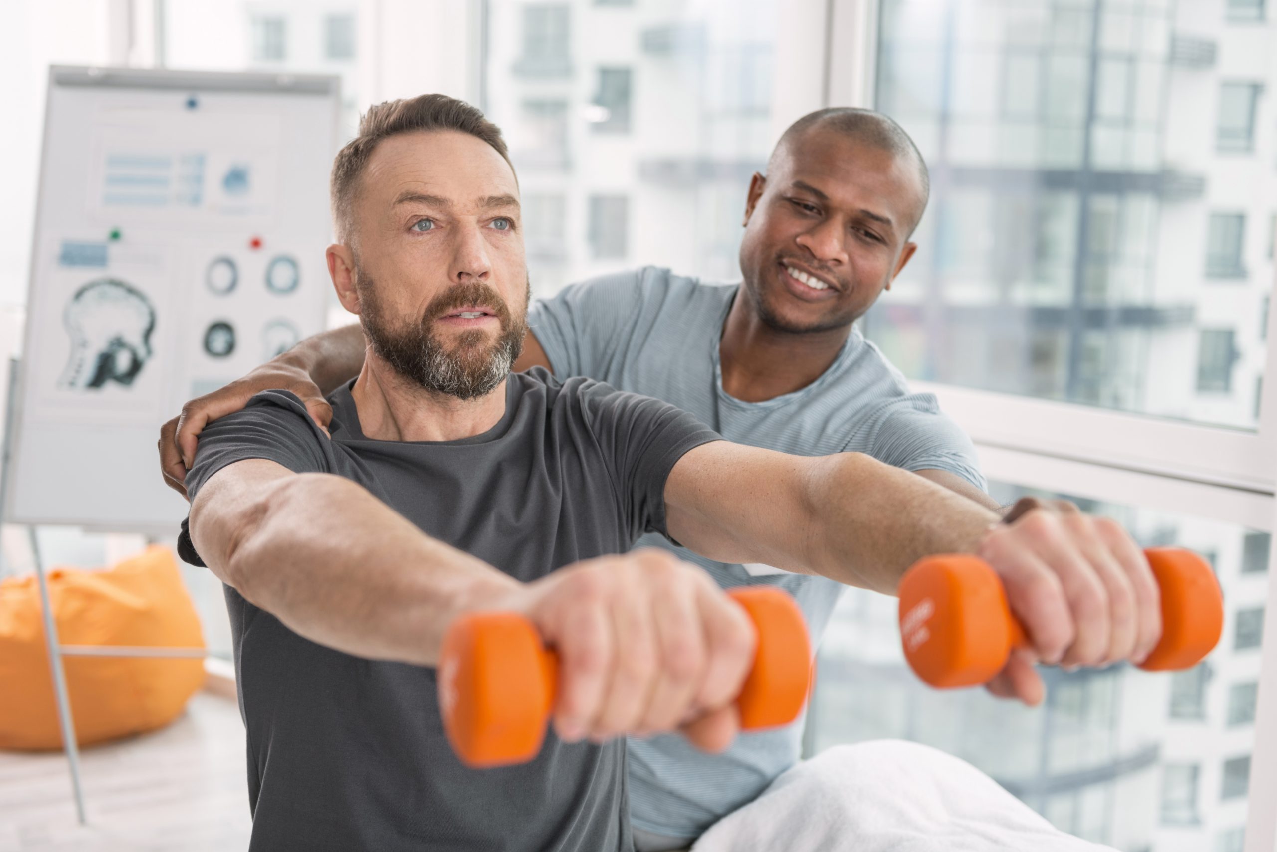 Adult person wearing a tank top, holding dumbbells in front of him while exercising indoors.