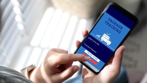 A person is holding a smartphone displaying a package tracking app. The screen shows the package's journey from New York, USA, to London, England, with a field for entering a tracking number.