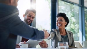 A group of business professionals smiling and shaking hands during a meeting in a bright, modern office.