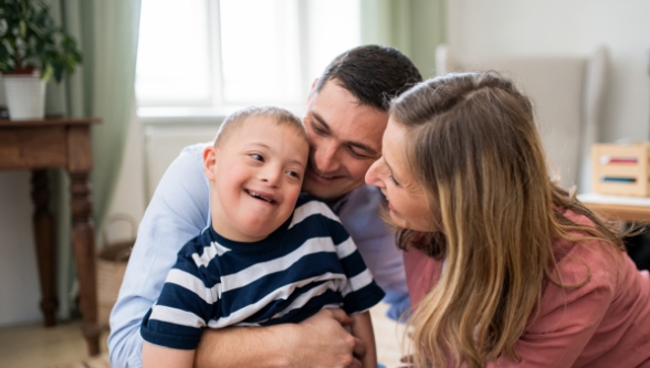 A mother and father smiling at their child who has Down syndrome.