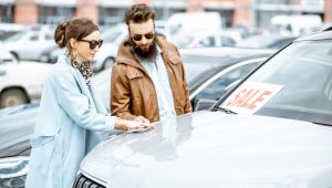 A young couple looking at a used car in a dealership lot.