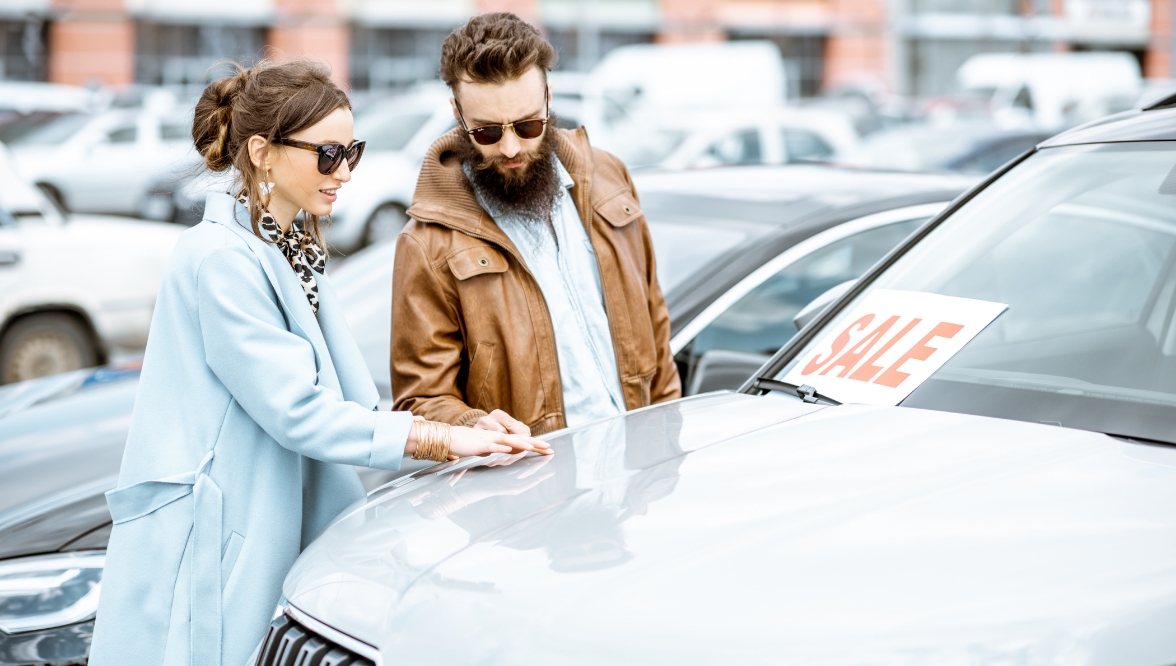 A young couple looking at a used car in a dealership lot.