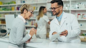 An older woman consults a male pharmacist, who shows her information on a document.