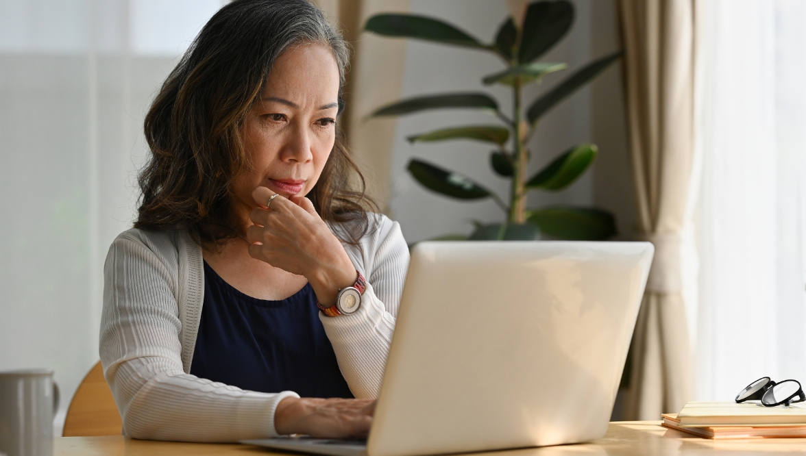 Woman thoughtfully looking at a laptop at home.
