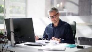 A man with gray hair works at a desk in an office, reviewing documents.