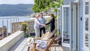 A couple greeting a real estate agent on the deck of a waterfront home with scenic views.
