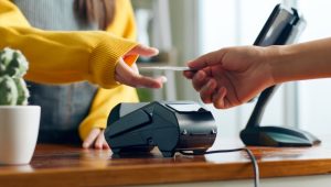 A woman in a yellow sweater takes a credit card from a customer.