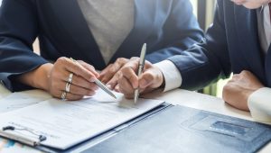 An individual in a blue suit indicates to another person, also in a blue suit, the place for their signature on a contract.