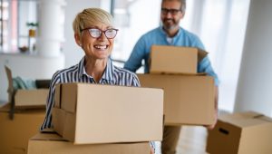 Smiling older couple carrying cardboard boxes while moving into a new home.