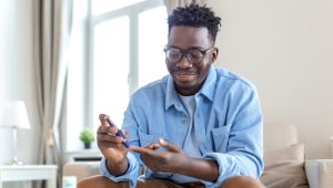 Smiling man checking his blood sugar with a glucometer, managing his diabetes at home.