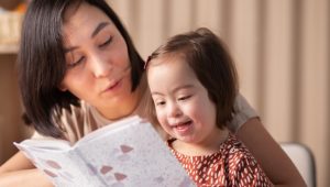 Woman reading a book with a smiling young girl with Down syndrome.