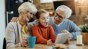 Smiling grandparents and child enjoying looking at a tablet together at home.