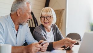 Smiling older couple using a smartphone and laptop together at a table.