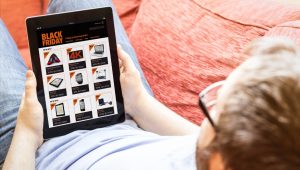 Man browsing Black Friday deals on a tablet while sitting on a couch.