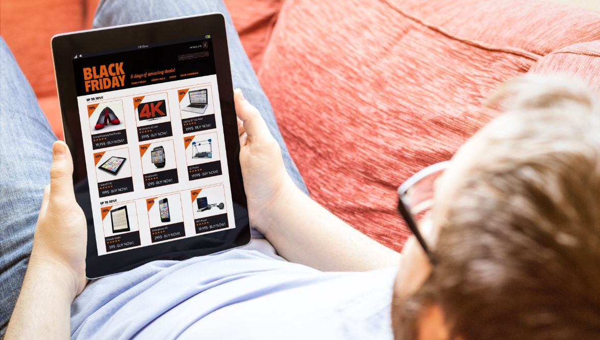Man browsing Black Friday deals on a tablet while sitting on a couch.