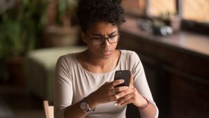 A young woman in a pink T-shirt scowls at her smartphone.
