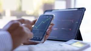 Disembodied hands hold a smartphone showing a graph; nearby is a tablet with other graphics.