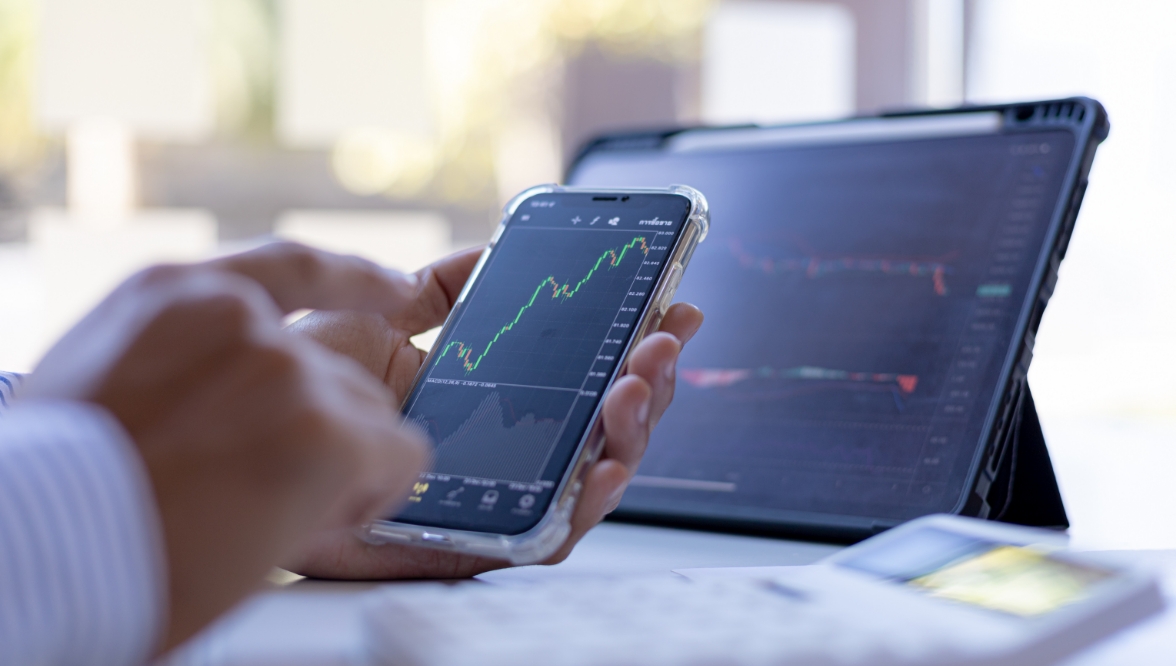Disembodied hands hold a smartphone showing a graph; nearby is a tablet with other graphics.